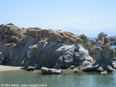 Swimmers climbing smooth granite boulders between sand and turquoise water