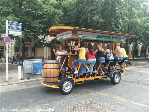 Group of tourists pedaling a yellow beer bike with wooden barrel through Berlin