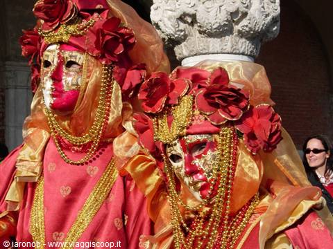 Two figures in red and gold costumes with golden masks at Venice Carnival