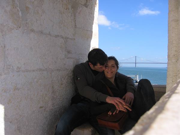 young couple sitting by stone wall with suspension bridge over the river behind