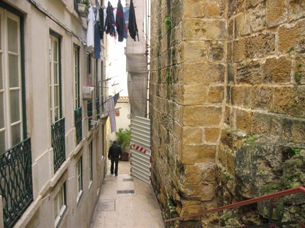 Narrow Lisbon alley, laundry hanging overhead, man walking beside old stone wall
