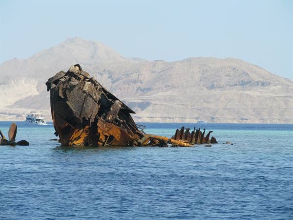 Rusted shipwreck half-submerged in turquoise water, desert mountains behind