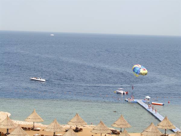 Straw umbrellas on beach, pier over blue sea, boat towing a parasail