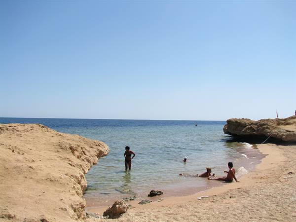Bathers in turquoise water between sandy rocks on a Red Sea beach