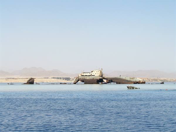 Rusty shipwreck grounded in turquoise water, arid mountains on the horizon