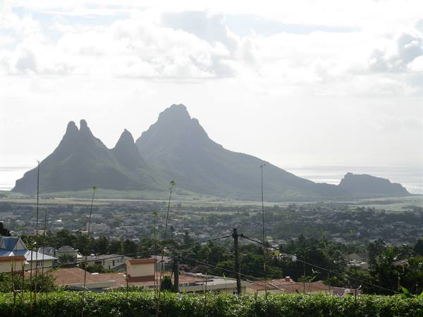 The Trois Mamelles peaks above town, rooftops and shrubs in the foreground