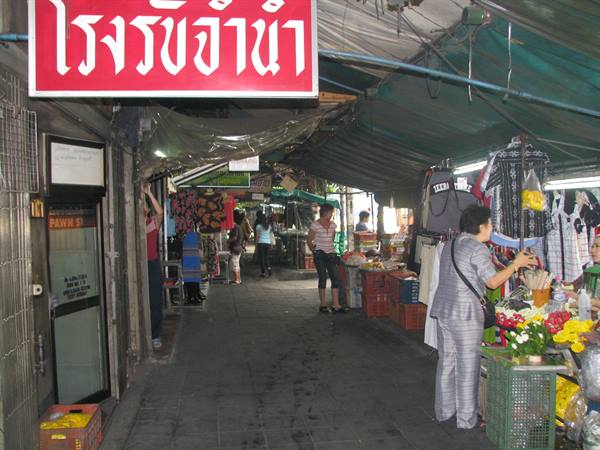 Covered market in Bangkok, woman browsing flowers and clothes under tarps