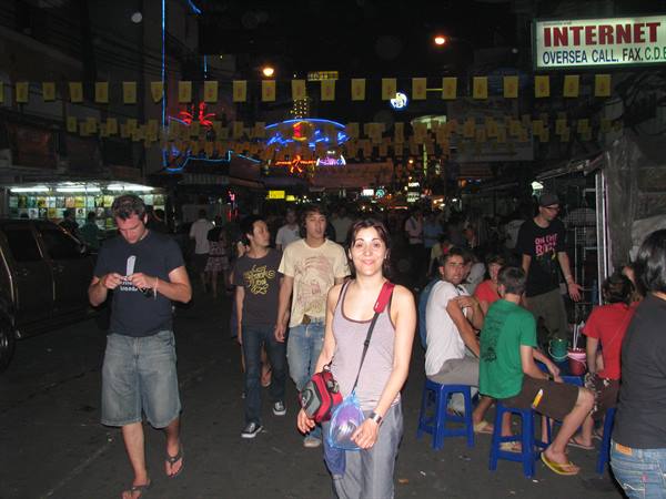 Smiling tourist with red bag walking through night crowd under neon signs