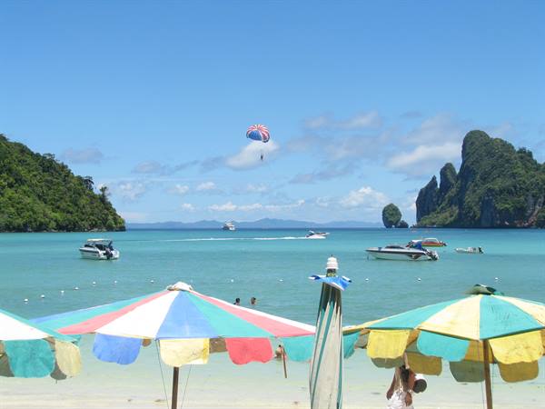 Colorful umbrellas on Phi Phi beach, parasailing boat and limestone karsts