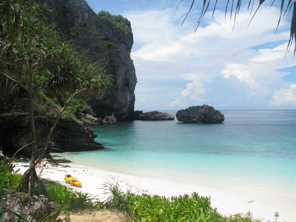 White sand beach with yellow kayak beneath limestone cliff, turquoise water
