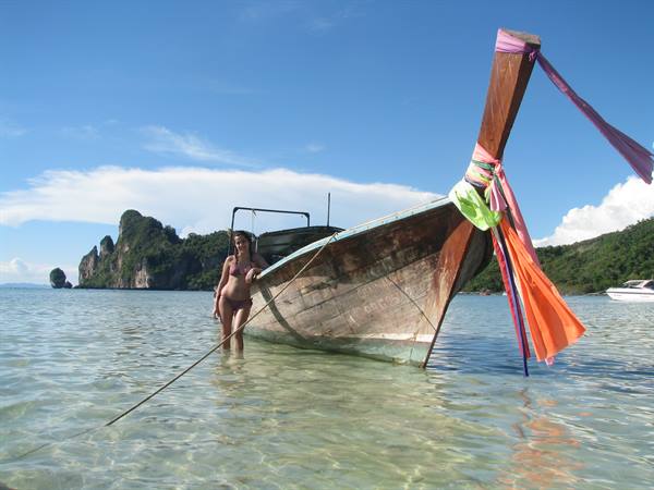 Woman in bikini moors a wooden longtail boat in turquoise shallows, limestone karsts behind