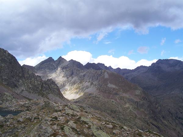 Granite peaks under clouds, small lake at left, rocky trail in foreground