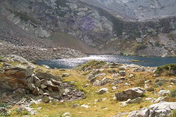 Alpine lake amid granite boulders, yellow grass and sparkling water in sunlight