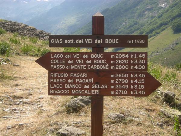 Wooden trail signpost with hiking directions to alpine lakes and refuges, green mountains behind