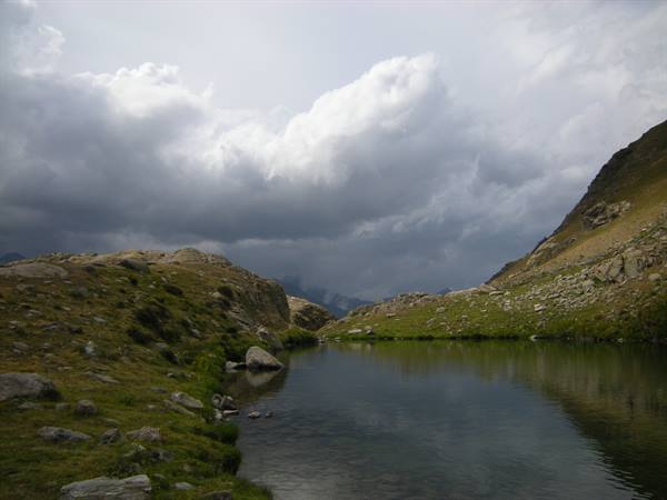 Alpine lake surrounded by rocks and grassy slopes, cloudy sky