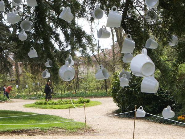 White ceramic cups hanging from pine branches in a public garden
