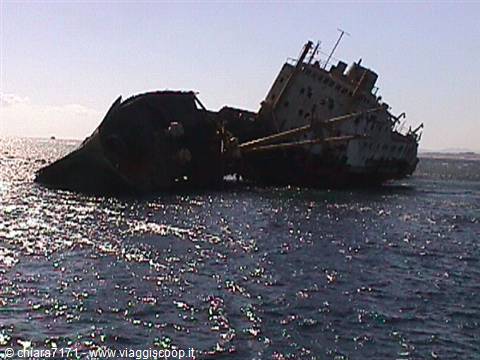 Rusty wrecked ship half-sunken, tilting on sparkling sunlit water