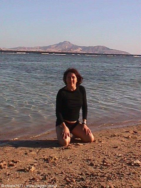 Woman kneeling on wet sand by the sea, arid mountains in background