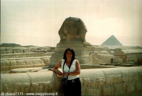 Woman leaning on stone wall in front of the Sphinx and Great Pyramid