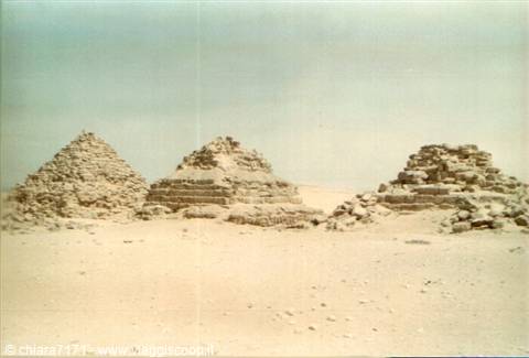 Small stepped stone pyramids in Giza desert under pale sky