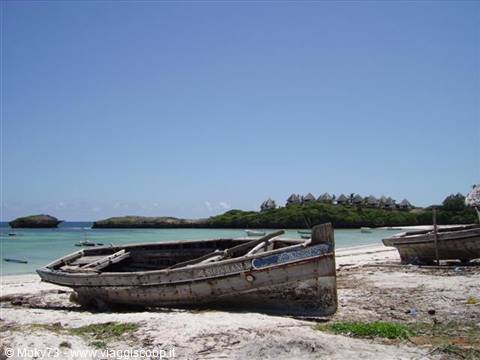 Weathered wooden fishing boats stranded on white sand, resort on the headland