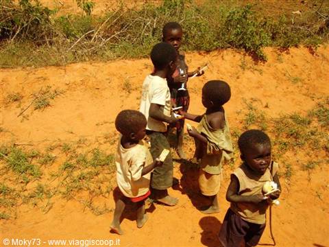 African children standing on red dirt, one eating a fruit
