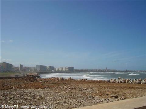 Ocean waves before the city buildings, rocky shore in the foreground