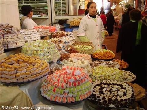 Vendor surrounded by colorful traditional sweets in Marrakech souk