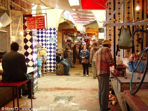 Tourists inside Marrakech covered souk among stalls and checkered tiles