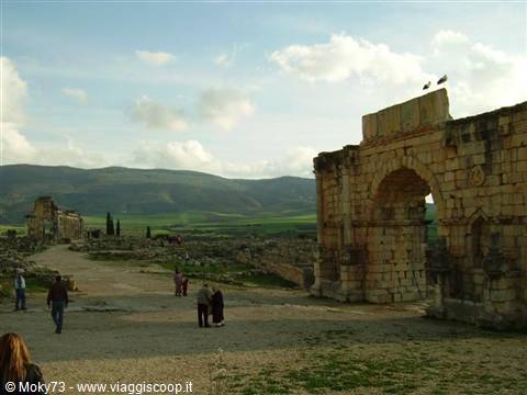 Tourists walk among Roman ruins of Volubilis near the triumphal arch