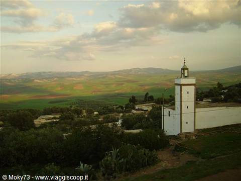 White minaret above green fields and rolling hills, cloudy sky