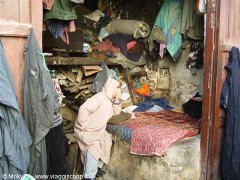 Hooded man in a poor room with blankets and hanging clothes