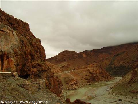 Green river winding through red rock gorge, road climbing under cloudy sky