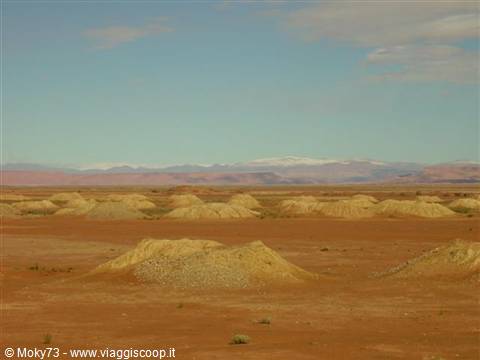 Piles of sandy earth on red hammada, snowy mountains on the horizon