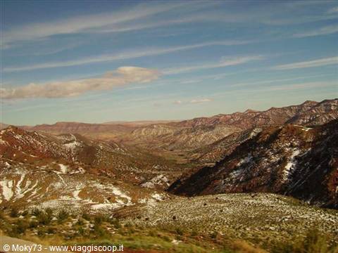 Red High Atlas mountains with snow and green valley under white clouds
