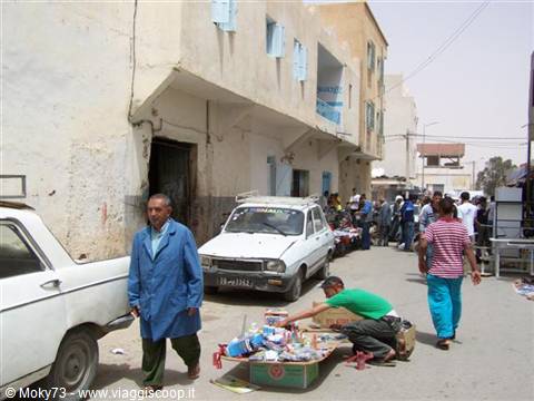 Street vendor selling goods on the ground along a dusty road with white buildings