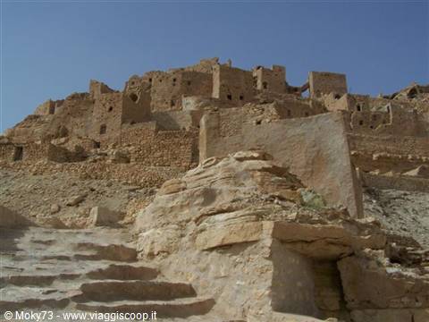 Ancient mud-brick Berber village on rocky hill, stone staircase under clear blue sky