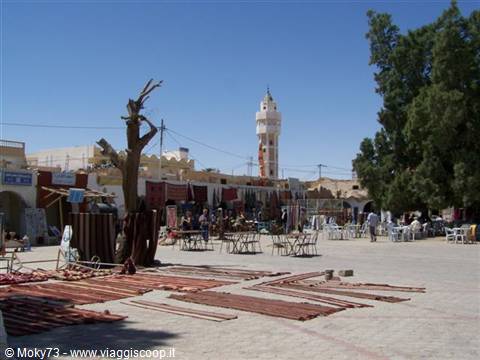 Douz market: carpets for sale, white minaret and shaded café tables