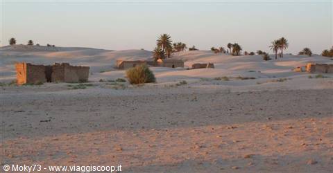 Mud-brick ruins among sand dunes and palm trees in the desert