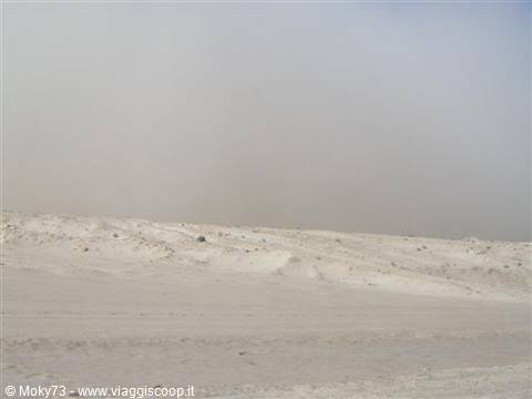 White desert sand blown by wind under a pale sky
