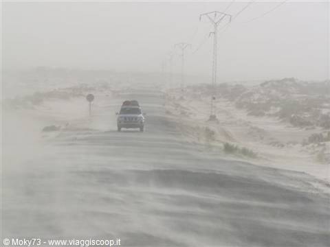 Car on coastal road during sandstorm, power pylons in the haze