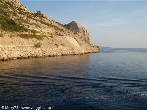 White rocky cliff above calm sea, coastal road carved into stone