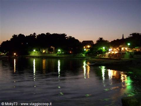 Restaurant lights and lamps reflected on calm bay water at dusk