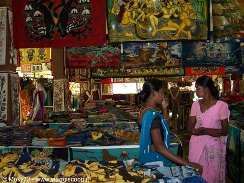 Women in saris among colorful batik stalls, warm light inside market