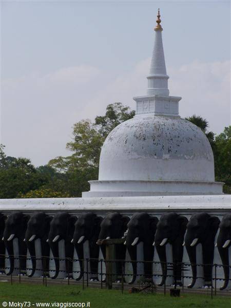 White stupa with golden spire, ringed by stone elephant statues