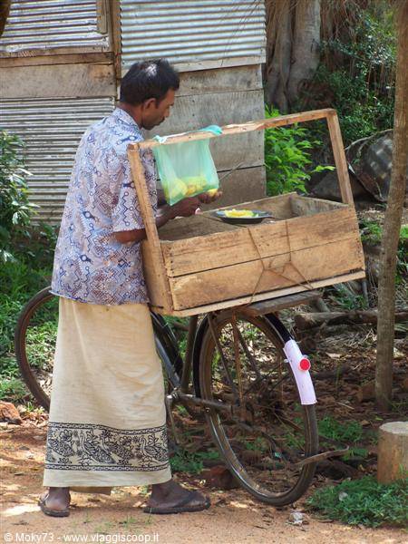Vendor in sarong beside a bicycle loaded with wooden crates