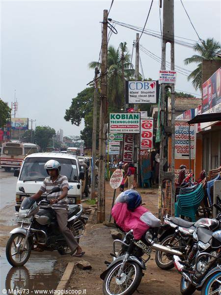 Helmeted motorcyclists and parked scooters along a wet street lined with shops