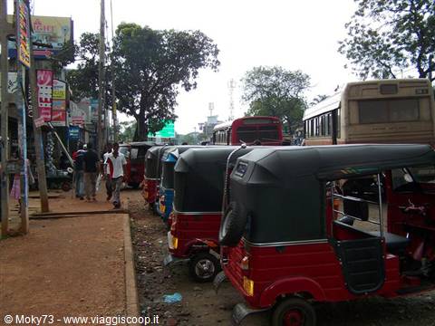 Row of red tuk-tuks parked along a dusty street