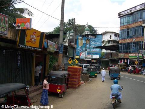 Busy street with red tuk-tuks, motorbike and mosque minaret in background