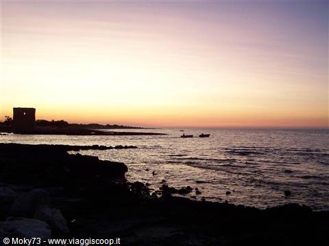 Boat silhouetted beside a coastal watchtower at dusk